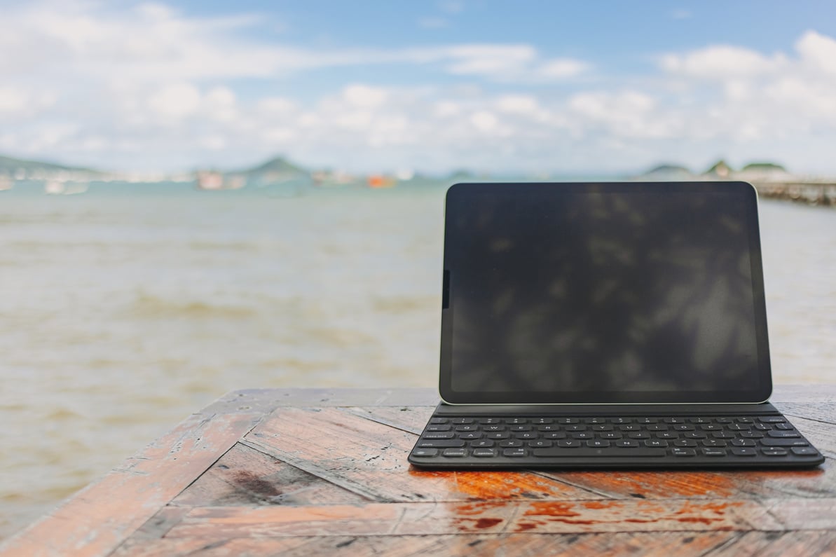 Black Tablet with Keyboard on Table and Sea View in Concept of Workation.